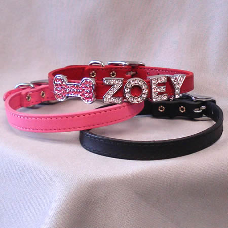 Stack of red, pink, and black dog collars with charms on the red, including a bone in pink crystals and the name "ZOEY" in clear crystals.